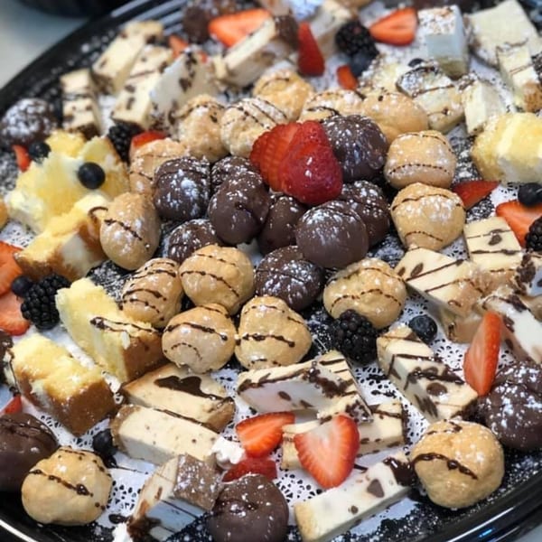 A dessert platter with various pastries, chocolate-covered treats, fresh berries, and powdered sugar.