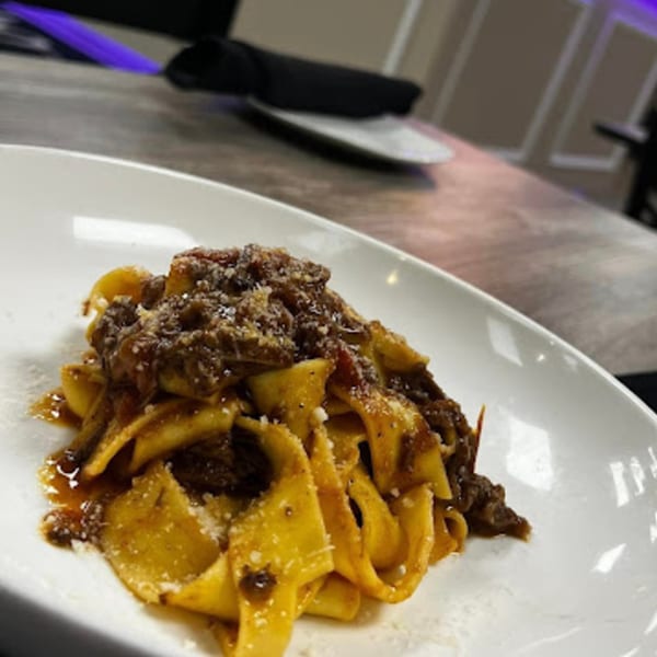 Cibo by Illiano's pappardelle pasta with a rich meat ragu and grated cheese on a white plate.