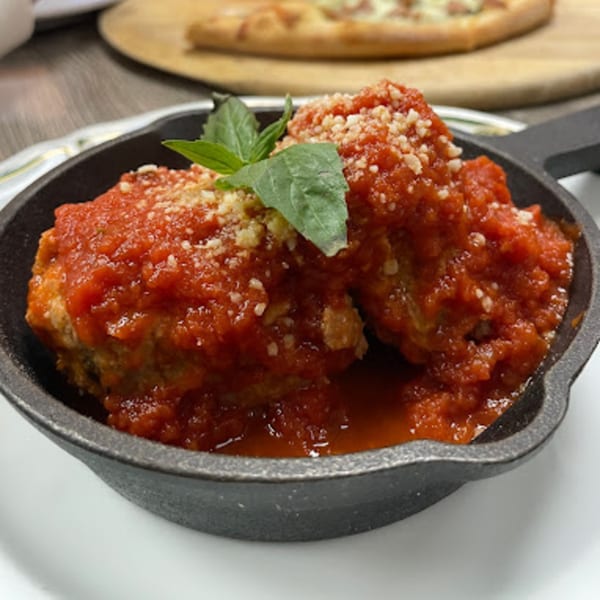Two meatballs in a cast iron skillet, covered in red sauce, parmesan, and basil.