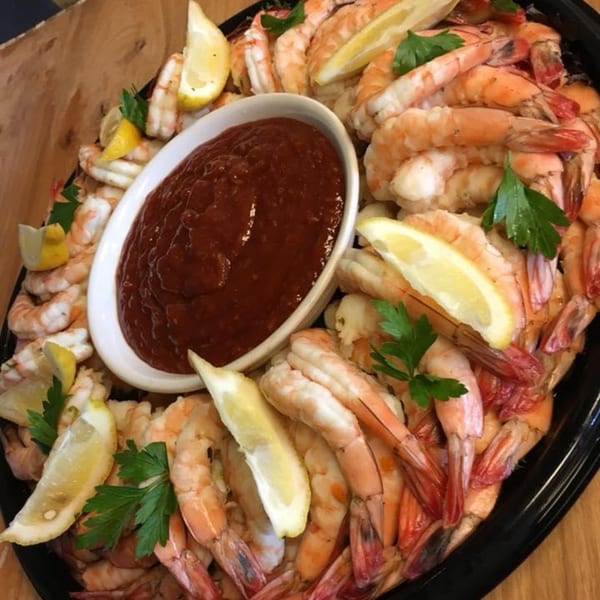 A large platter of cooked shrimp with lemon wedges, parsley, and a bowl of cocktail sauce.