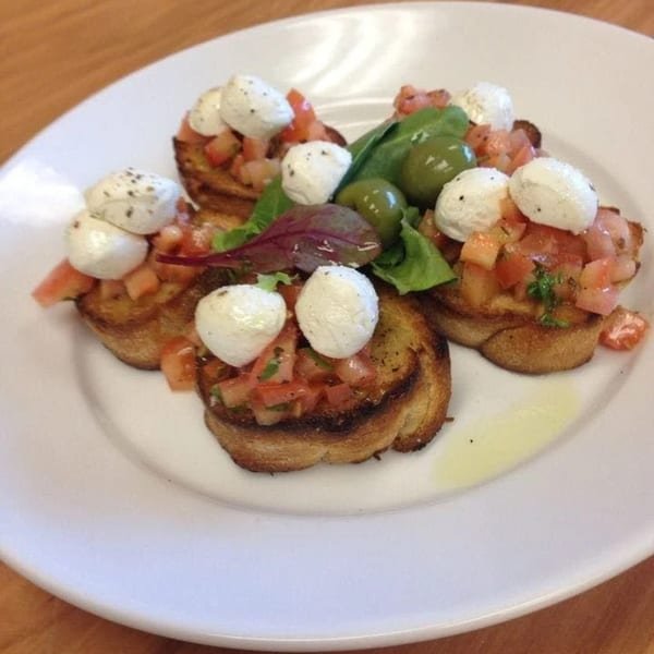 Italian bruschetta with diced tomatoes, mozzarella balls, olives, and greens on a white plate.
