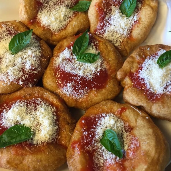 Close-up of golden-fried Italian dough topped with red sauce, grated cheese, and fresh basil.